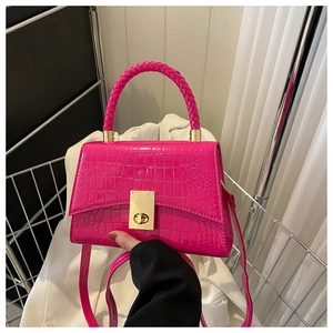 Detail of rose pink crocodile embossed handbag with woven handle and gold twist lock