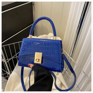 Detail of royal blue crocodile embossed handbag with woven handle and gold twist lock