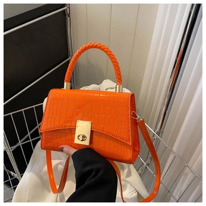 Detail of bright orange crocodile embossed handbag with woven handle and gold metal lock