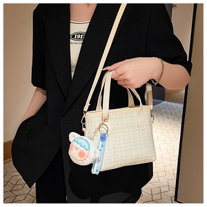 Dettaglio della borsa a secchiello in tweed bianco con ciondolo cartoon e tracolla