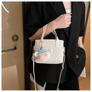 Dettaglio della borsa a secchiello intrecciata beige con ciondolo a forma di bambola