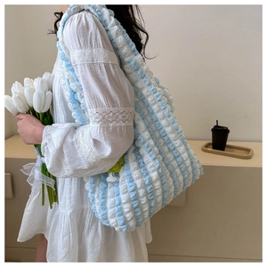 Detail of blue striped bubble tote bag with yellow flower pendant on model's shoulder