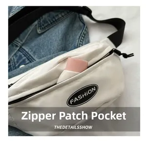 Gros plan sur la poche avant zippée du sac banane blanc montrant sa capacité de rangement