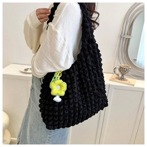 Detail of black popcorn texture tote bag featuring a yellow flower charm and green chain