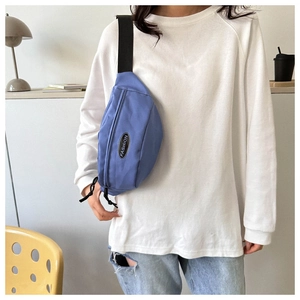 Close-up of blue nylon crossbody bag with adjustable strap and Fashion label on model