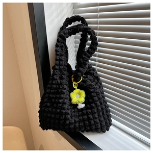 Detail of black popcorn texture tote bag featuring a bright yellow flower charm accessory