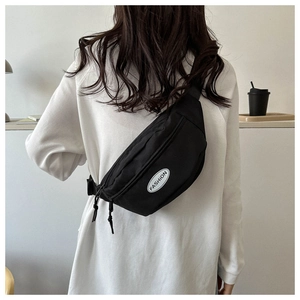 Model wearing a minimalist black nylon waist bag with a white Fashion logo patch