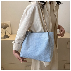 Detail of light blue woven texture tote bag with slim leather straps on shoulder