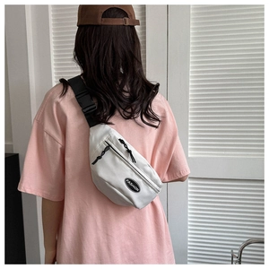 Detail of white nylon crossbody bag with fashion patch and adjustable strap on a model