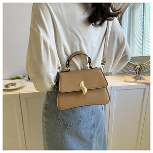 Détail d'un sac bandoulière beige structuré avec une boucle dorée en flamme