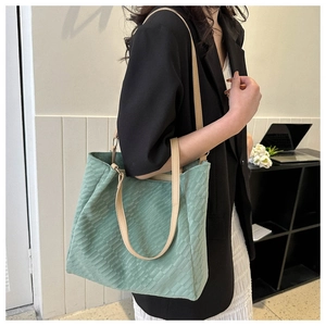 Detail of mint green corduroy tote bag with beige straps worn by a model in a modern room