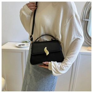 Détail du sac trapèze noir élégant avec un fermoir doré ondulé unique et une poignée