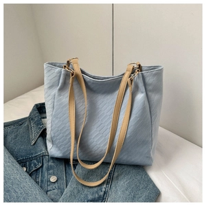 Detail of light blue textured tote bag with khaki leather handles on denim background