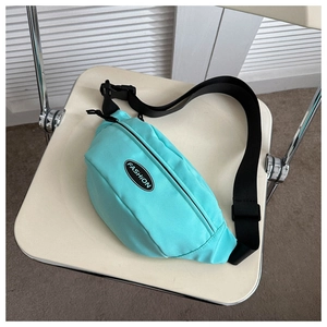 Detail of teal green casual fanny pack with black adjustable strap on an ivory chair