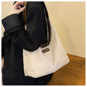 Close-up of quilted cream tote bag with brown leather trim and shoulder strap detail