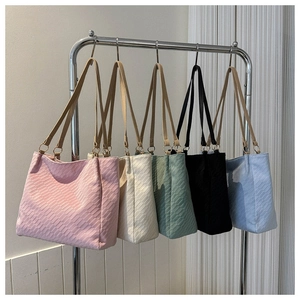 Five assorted colors of woven texture tote bags hanging on a metal display rack
