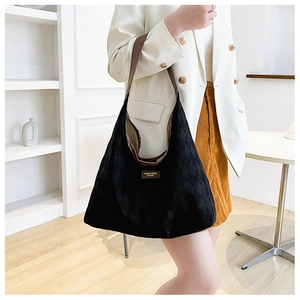 Detail of black quilted tote bag with brown leather strap and brand logo patch