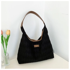 Detail of black quilted canvas tote bag with brown faux leather handles and logo plate