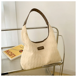 Detail of beige quilted canvas tote bag with brown leather strap on a minimalist shelf