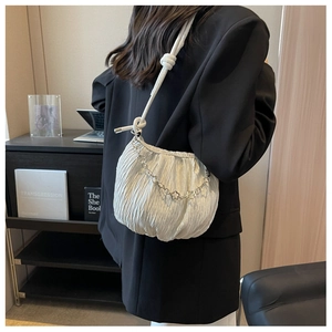 Detail of white pleated shoulder bag featuring silver flower chain and knotted strap