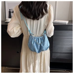 Detail of light blue pleated cloud bag with silver floral chain on a shoulder strap