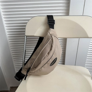 Minimalist beige crossbody bag with adjustable black strap displayed on a white chair