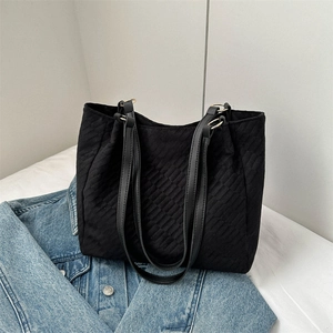 Black quilted tote bag with leather straps and gold rings on denim background
