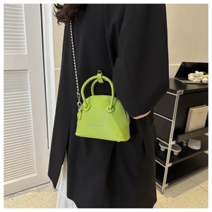 Close-up of a neon green textured leather shell bag with a silver chain strap on a black blazer