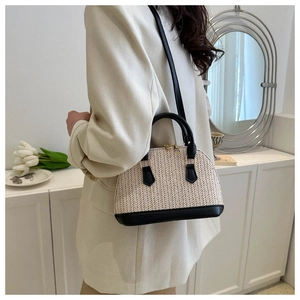 Detail einer beige gewebten Muscheltasche mit schwarzen Ledergriffen und Goldreißverschluss