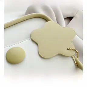 Detail of flower charm with gold chain and circular leather buckle on white saddle bag