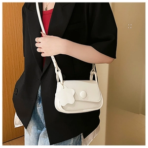Detail of off-white crossbody bag with matte leather finish and floral pendant on strap