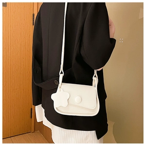 Close-up of white minimalist flap crossbody bag with a decorative flower charm and round buckle