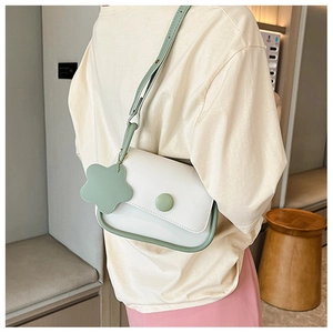 Detail of minimalist cream crossbody bag with green trim and floral pendant accessory