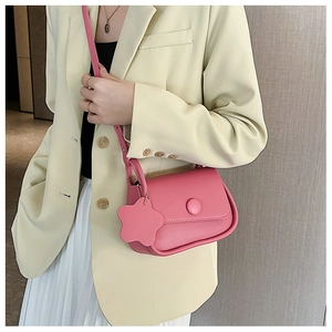Pink leather square crossbody bag with floral charm worn on light yellow suit blazer