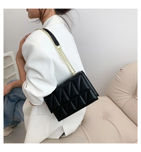 Detail of black quilted crossbody bag with gold chain strap worn by a model