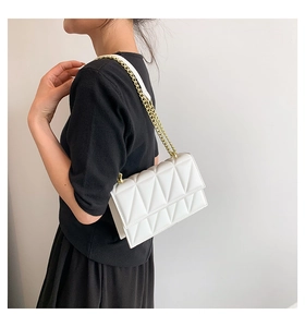 Detail of white geometric quilted crossbody bag with golden chain strap on a model