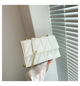 Detail of white quilted leather texture and gold chain strap on a small flap bag