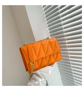 Detail of bright orange quilted chain bag with geometric stitching and gold hardware