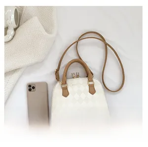 White quilted shell bag with brown leather handles and gold zipper next to a phone