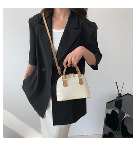 Quilted cream shell bag with brown handles carried by a model in casual attire