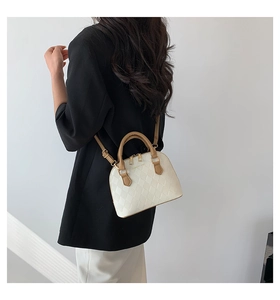 Detail of mini beige shell bag with quilted pattern and brown handles on model