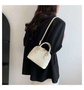 Detail of cream-colored checkered shell bag with top handles and adjustable shoulder strap