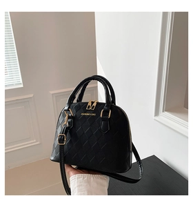 Detail of black quilted shell crossbody bag with gold hardware and brand logo lettering