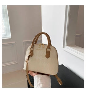 Close-up of beige shell bag with quilted texture, brown handle, and gold-tone zippers