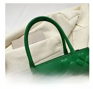 Detail view of green leather handbag featuring clover textured embossing and sturdy handles