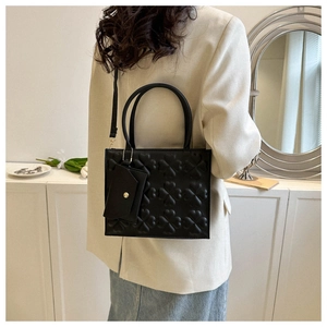 Close-up of black crossbody bag featuring embossed clover texture and mini envelope pouch