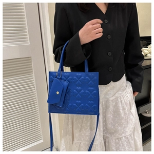 Detail of blue embossed crossbody bag with matching heart charm shown on model