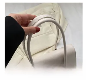 Close-up of cream leather shoulder bag featuring a slim rectangular design and long handle