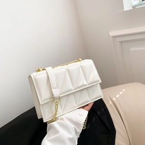 White quilted chain shoulder bag with geometric stitching held by model in minimalist setting