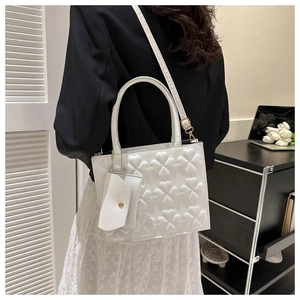 Model wearing a white crossbody bag with embossed clover patterns and gold hardware